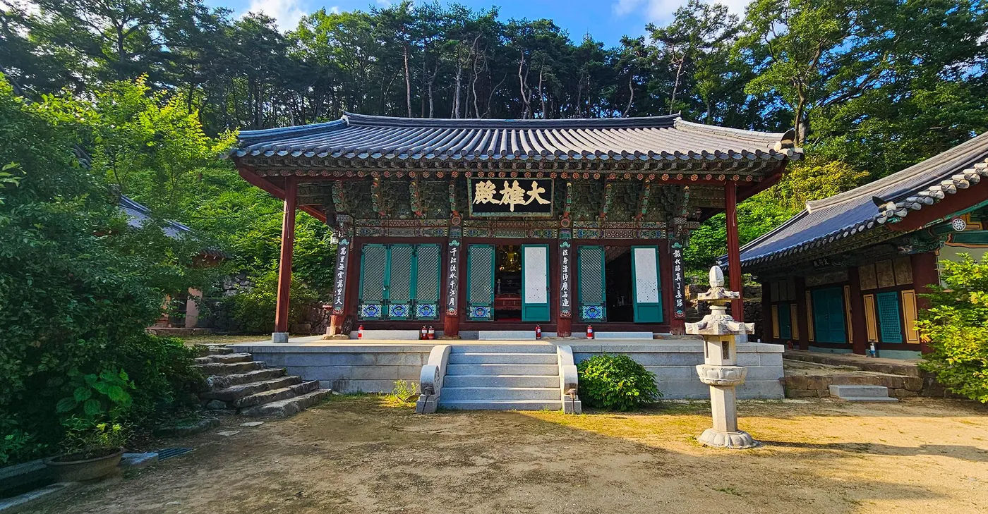 초록 숲에 둘러싸인 대웅전(현판 大雄殿) 정면과 돌계단, 석등, 모래 마당
